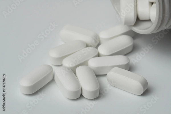 Fototapeta White pills tablets spilled from a bottle on a light grey background close up