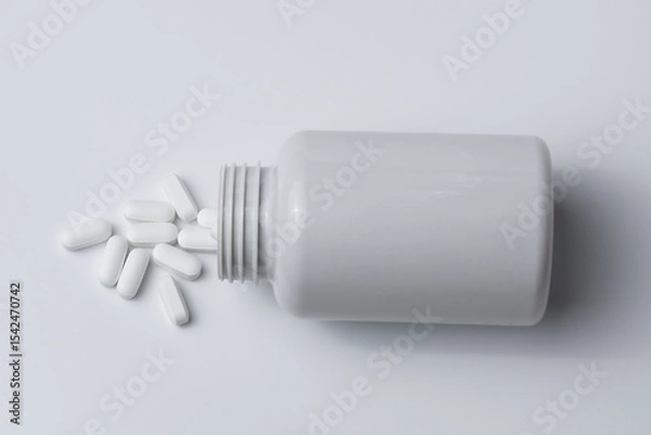 Fototapeta White pills spilled from a bottle on a light grey background top view
