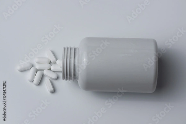 Fototapeta White pills spilled from a bottle on a light grey background top view