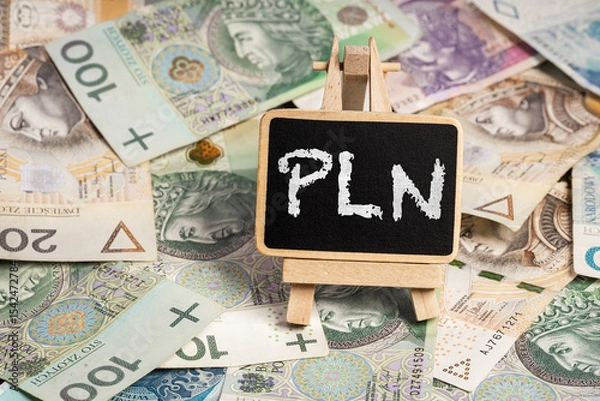 Obraz Black writing board on a wooden frame with the inscription "PLN", Polish zloty PLN banknotes scattered in the background (selective focus)