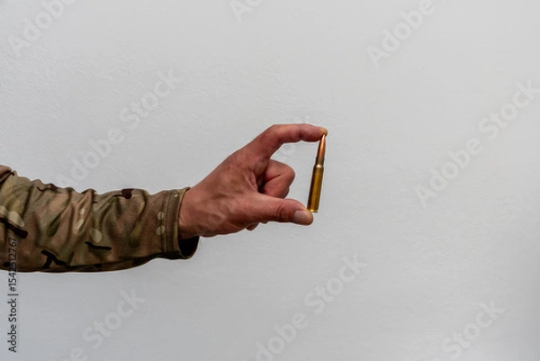 Obraz A single cartridge in the hand of a soldier. Minimalistic image conveying the theme of weaponry, war and the decisive shot.
