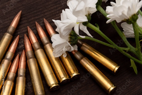 Obraz Flowers and bullets against a background of textured wood. The composition creates a powerful visual metaphor suitable for themes related to veterans, mourning, or the aftermath of war.