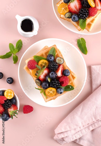 Fototapeta Crispy Belgian waffles with fresh berries and maple syrup on pink background. Top view.