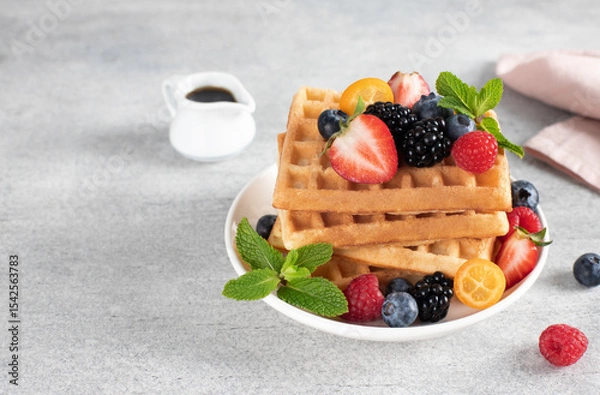 Fototapeta Crispy Belgian waffles with fresh berries and maple syrup on a gray background. Close-up, copy space.