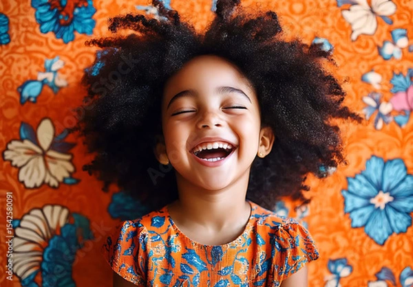 Fototapeta Joyful child with afro hair laughing against a vibrant floral background