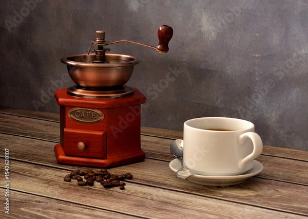 Obraz A manual coffee grinder, fried grains and a cup of freshly brewed black coffee on a wooden table.
