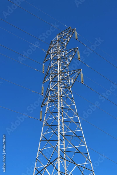 Fototapeta Looking upwards at a transmission tower and electricity power lines against a clear blue sky