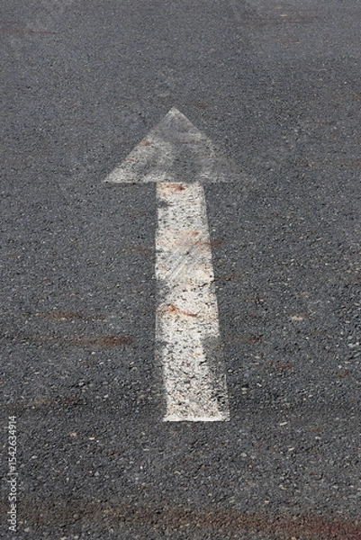 Fototapeta Weathered white arrow pointing straight ahead painted on a road asphalt surface
