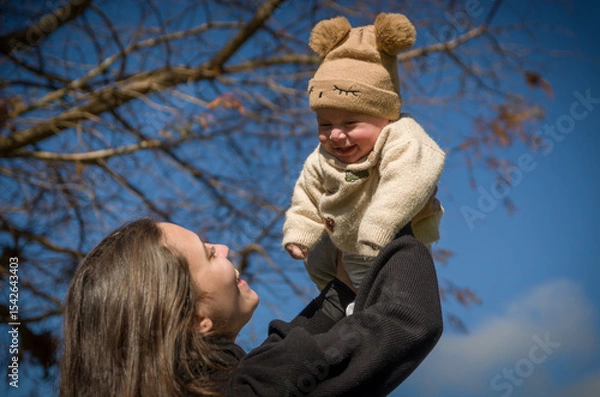 Fototapeta Mother playing with son in sunny square throwing him up while he smiles