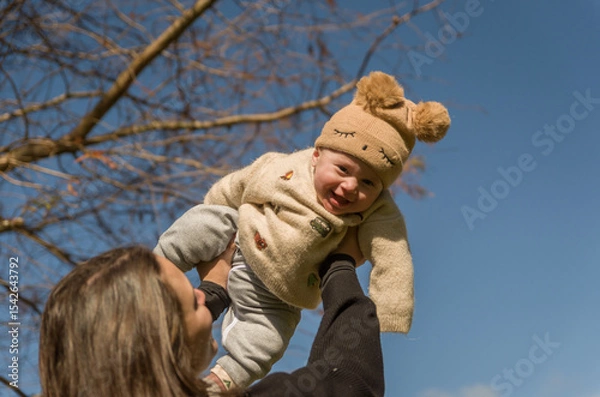 Obraz Mother playing with son in sunny square throwing him up while he smiles