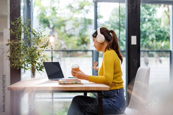 Obraz Happy asian girl college student wearing headphones watching distance online class, remote university webinar or having talk on laptop video conference call virtual meeting at home or campus.
