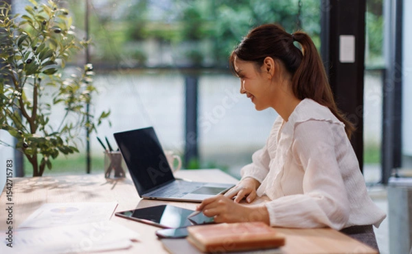 Obraz Young Asian professional business woman office worker analyst sitting at desk working on laptop thinking on project plan, analyzing marketing or financial data online, watching elearning webinar.	
