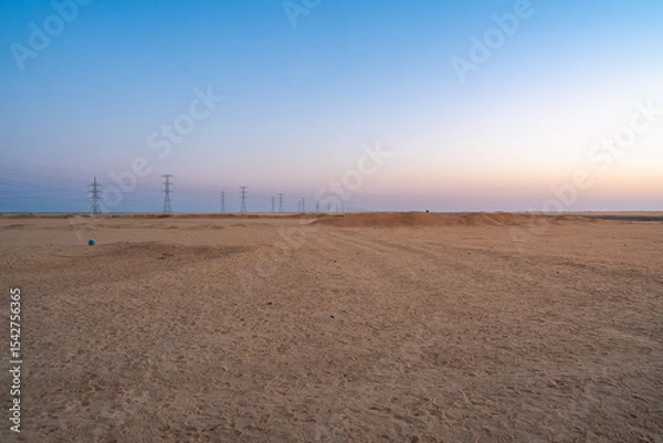 Obraz The tranquil Aswan desert in Egypt at dawn, featuring a gentle sunrise glow and a series of electricity pylons stretching across the vast landscape on the journey to Abu Simbel Temples.