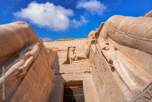 Obraz A dramatic low-angle view of the entrance to the Great Temple of Ramses II at Abu Simbel, Aswan, Egypt, showcasing the colossal statues and intricate carvings under a bright sky.