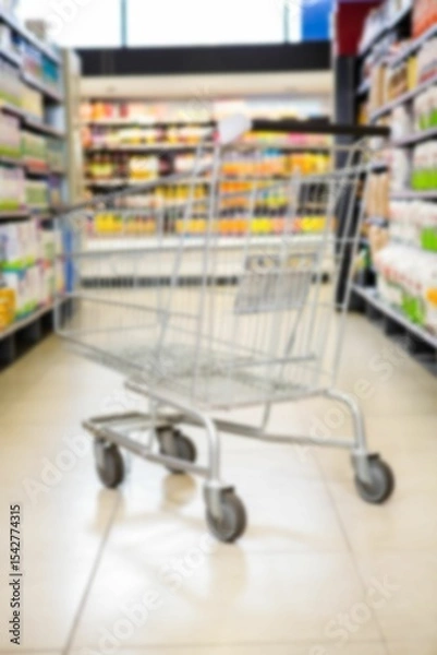 Obraz Shopping cart on aisle amidst products on shelves in supermarket
