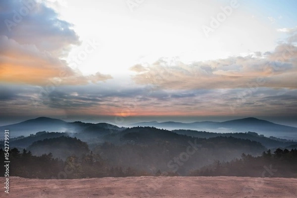 Fototapeta Misty hills and rocky plateau edge are featuring flat design with sun rays and mist layers