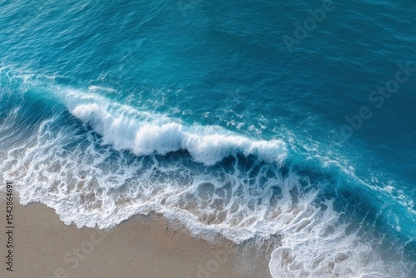 Fototapeta A wave crashes on a sandy beach creating white foam and blue water