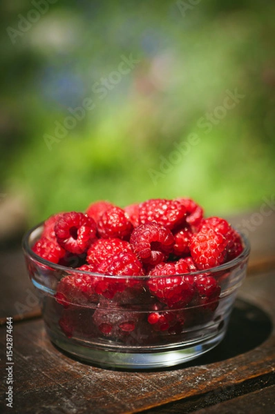 Fototapeta Transparent plate with juicy sweet raspberries on wooden table