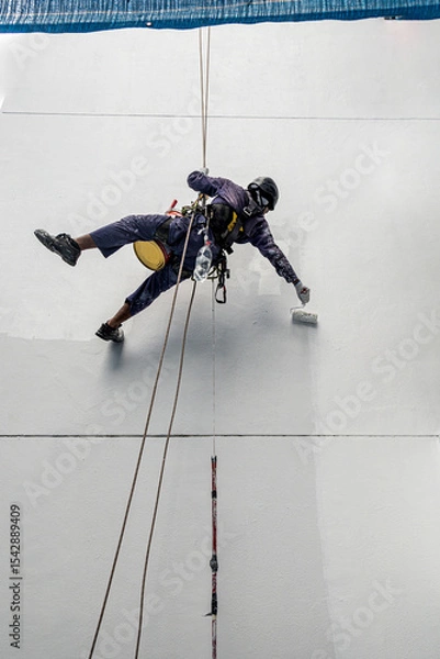 Fototapeta Real life worker labour painter construction worker climbing up hanging on wall painting the building wall