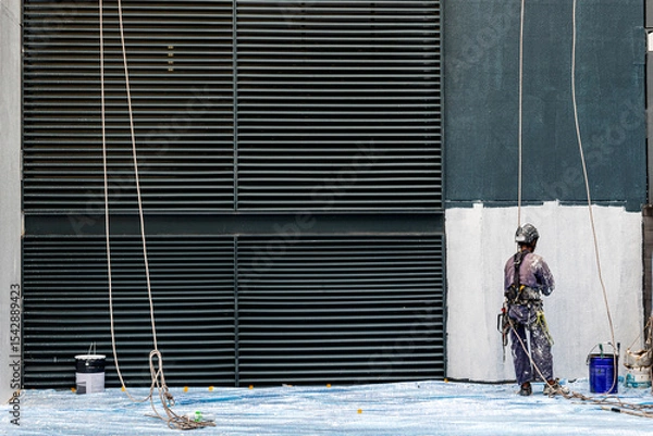 Fototapeta Real life worker labour painter construction worker climbing up hanging on wall painting the building wall