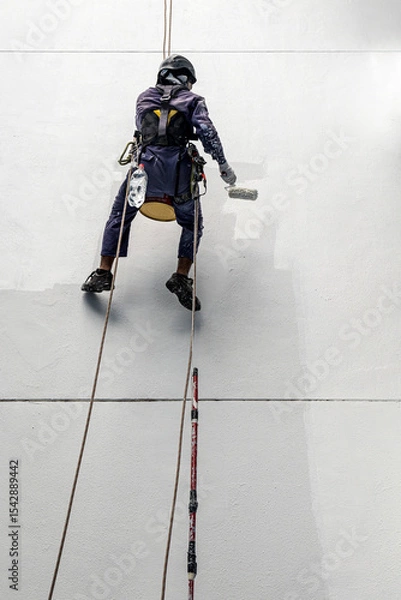 Fototapeta Real life worker labour painter construction worker climbing up hanging on wall painting the building wall