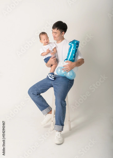 Fototapeta Father Holds One-Year-Old Child While Celebrating Birthday With Blue Balloon and Joyful ExpressionsFather Holds One-Year-Old Child While Celebrating Birthday With Blue Balloon and Joyful Expressions