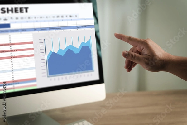 Obraz Man working on excel person pointing at computer screen displaying spreadsheet and line graph, analyzing data and trends in professional setting