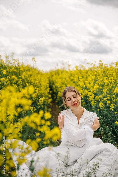 Fototapeta Woman enjoying a peaceful moment in a field of yellow flowers under a cloudy sky