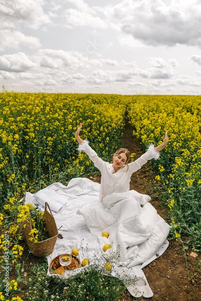 Fototapeta Woman enjoying a sunny day in a yellow flower field with lemons and picnic setup
