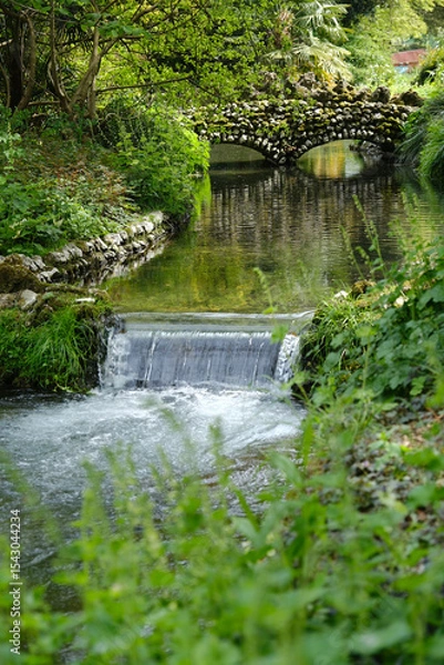 Fototapeta Small waterfall in the garden with stone bridge in the background, England