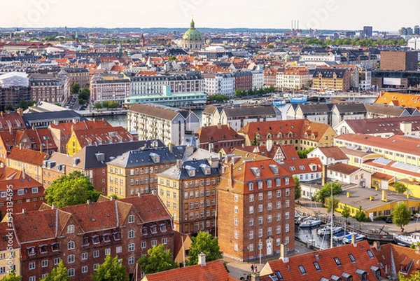 Fototapeta Panoramic view of Copenhagen taken from the top of the Church of Our Saviour, showing a mix of historical rooftops, modern buildings, and city landmarks under a warm evening sky.