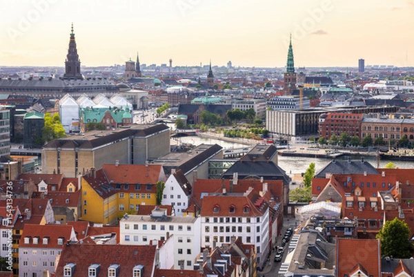 Fototapeta Panoramic view of Copenhagen taken from the top of the Church of Our Saviour, showing a mix of historical rooftops, modern buildings, and city landmarks under a warm evening sky.