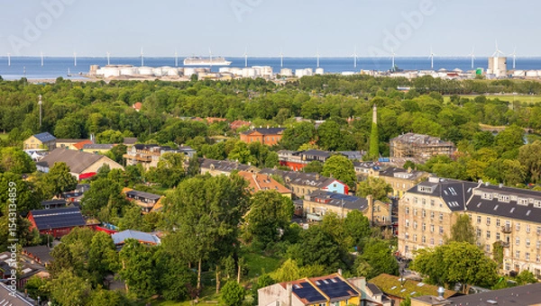 Fototapeta Panoramic view of Copenhagen taken from the top of the Church of Our Saviour, showing a mix of historical rooftops, modern buildings, and city landmarks under a warm evening sky.
