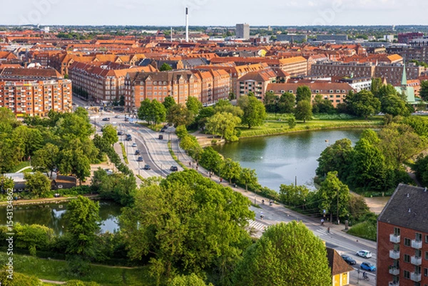 Fototapeta Panoramic view of Copenhagen taken from the top of the Church of Our Saviour, showing a mix of historical rooftops, modern buildings, and city landmarks under a warm evening sky.