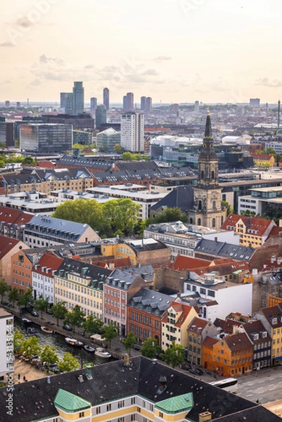 Fototapeta Panoramic view of Copenhagen taken from the top of the Church of Our Saviour, showing a mix of historical rooftops, modern buildings, and city landmarks under a warm evening sky.