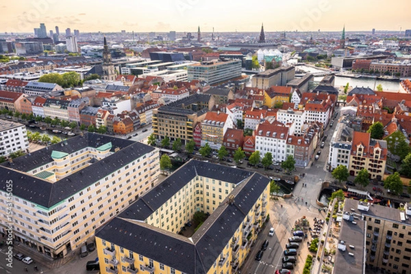 Fototapeta Panoramic view of Copenhagen taken from the top of the Church of Our Saviour, showing a mix of historical rooftops, modern buildings, and city landmarks under a warm evening sky.