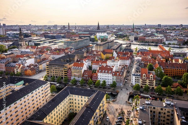Fototapeta Panoramic view of Copenhagen taken from the top of the Church of Our Saviour, showing a mix of historical rooftops, modern buildings, and city landmarks under a warm evening sky.