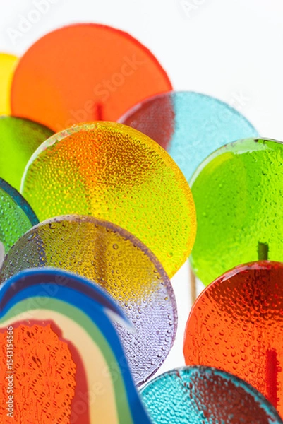 Fototapeta Macro shot of multi-colored caramel lollipops on the white background. Transparent candies on a wooden stick