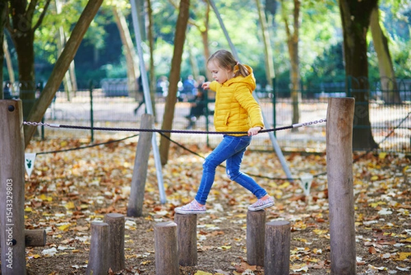 Fototapeta Cheerful little girl having fun on playground in autumn park in Paris, France.