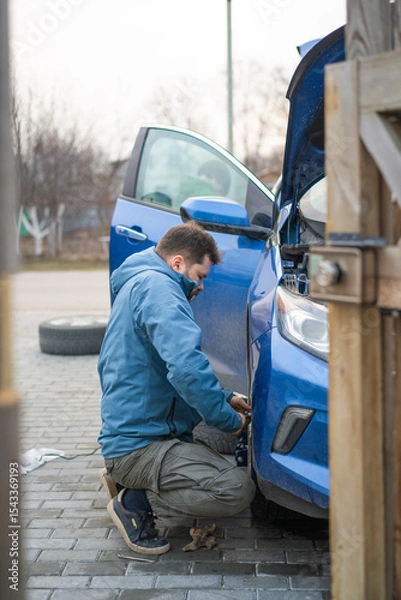 Fototapeta A man tightens the nuts on the wheel of a car
