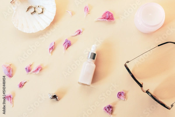 Fototapeta Face serum and women's accessories with dry peony petals on beige background. Top view, flat lay