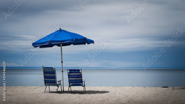 Fototapeta Beach chairs under an umbrella, soft light on sand. Peaceful summer escape by the ocean.