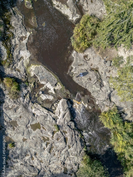 Fototapeta Aerial View of Rocky Riverbed with Person Sitting on Boulder