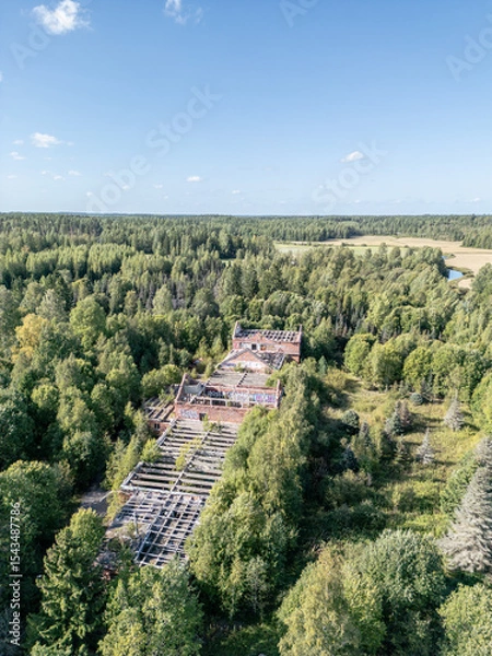 Fototapeta Aerial view of a long-abandoned brick structure hidden in the dense forest landscape. The roofless ruins are overtaken by nature.