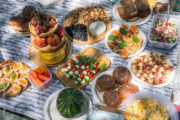 Fototapeta Summer Picnic Food Spread with fresh fruit, cheese platter, bread, and various appetizers arranged