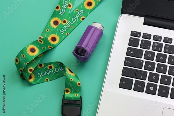 Fototapeta Hidden disability lanyard with a asthma device close to a laptop in a green background