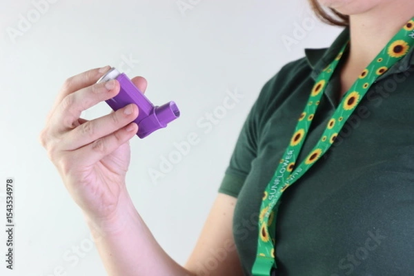 Fototapeta Woman worker holding a asthma device when wearing a hidden disability lanyard
