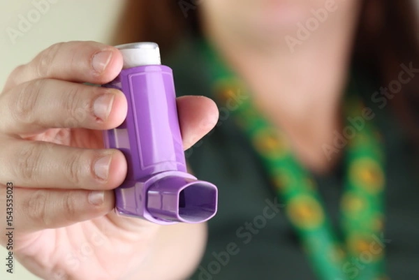 Fototapeta Woman worker holding a asthma device when wearing a hidden disability lanyard