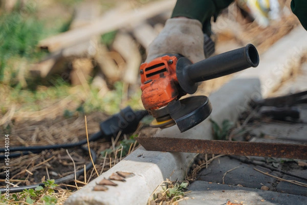 Fototapeta A man cuts off a piece of metal with a grinder. The power tool is in the hands of the master. Construction works.
