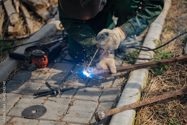 Fototapeta A man works with a welding machine. Sparks from welding. Joining metal parts using a welding machine.